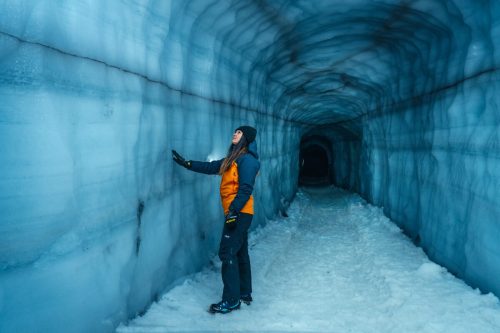 Lady wearing orange coat standing inside ice tunnel at Langjokull