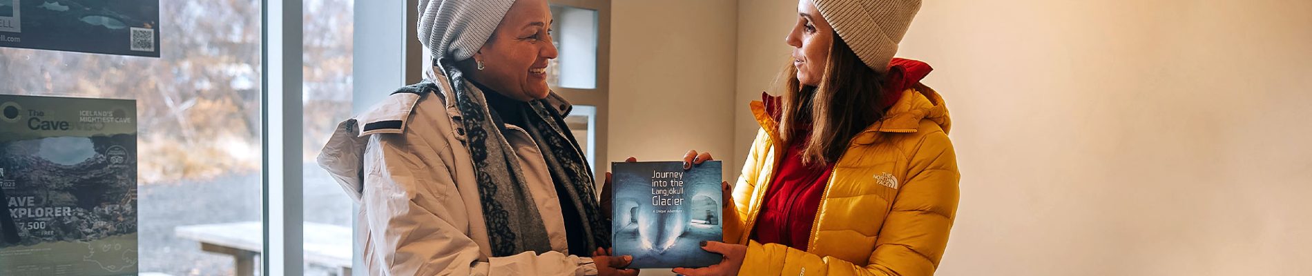 two women smiling and holding a book